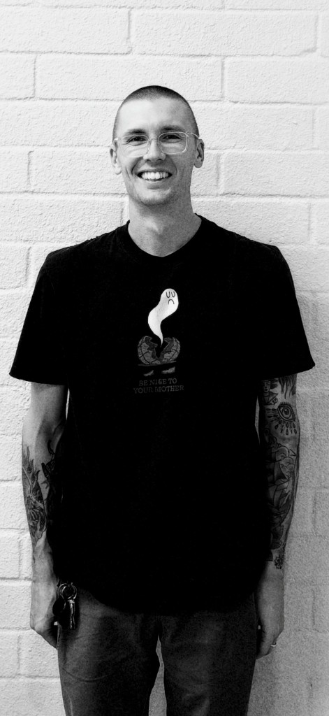 Lucas, barber at Trim Time, standing against a white brick wall