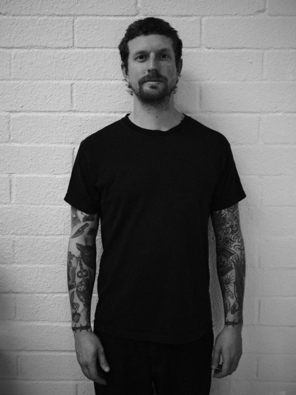Peter Danskin, barber and founder of Trim Time, standing against a white brick wall